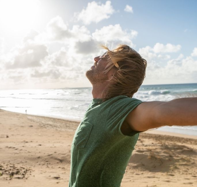 man with arms out relaxing on beach in florida